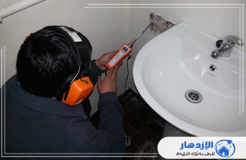 فني شركة الإزدهار 0505587508 يرتدي سماعات رأس ويستخدم جهاز كشف صوتي بجانب حوض الحمام، لتحديد مصدر تسرب المياه في المواسير المخفية. خدماتنا متاحة في العين.
