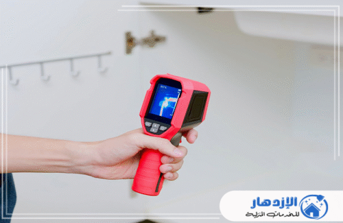صورة لفني يمسك بكاميرا حرارية حمراء متقدمة، يستخدمها لتحديد بقع الرطوبة المخفية في خزانة الحائط. شركة الإزدهار 0505587508 تقدم خدمة كشف تسربات المياه في العين بأحدث التقنيات.