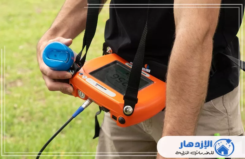 كشف تسربات المياه في ام القيوين 0505587508 الإزدهار رجل يحمل جهازًا برتقاليًا يحتوي على زر أزرق، يُستخدم في كشف تسربات المياه في أم القيوين.