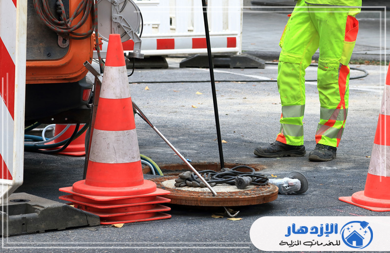 أفضل شركة تسليك مجاري راس الخيمة 0505587508 عامل شركة الازدهار يرتدي سترة صفراء يعمل على تسليك المجاري في الشارع.